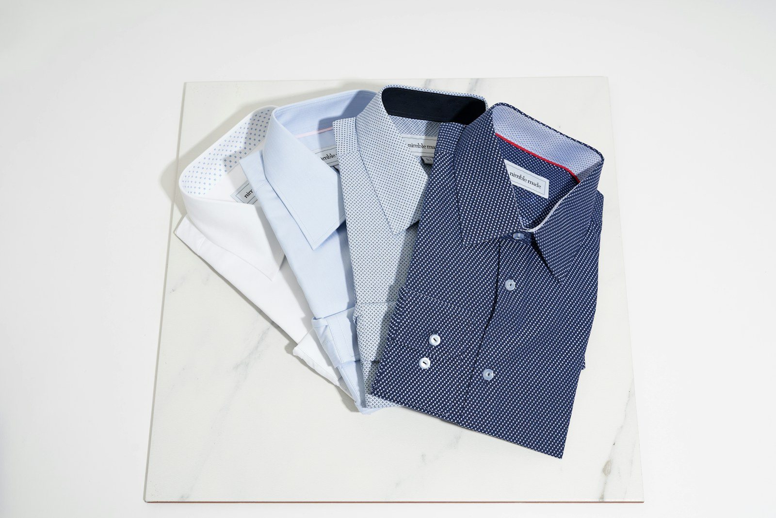 Camisas sociais dobradas em tons de branco e azul sobre mesa de mármore